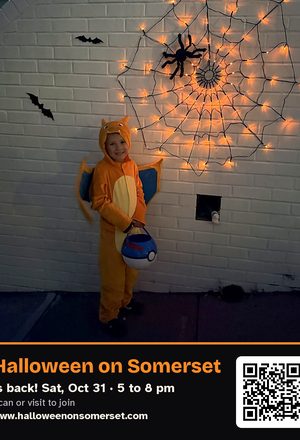 A trick-or-treater in a dragon costume by a glowing spider web, with event details & QR code